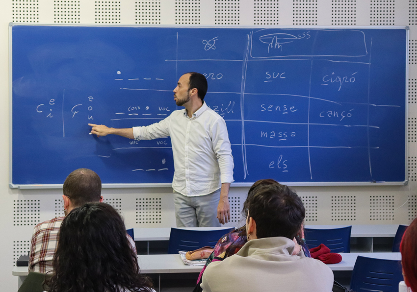 event image:Photo of the teacher pointing to a word written on the blackboard.